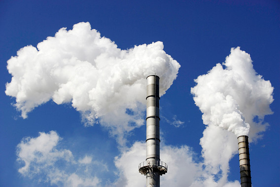Two industrial smokestacks emitting large plumes of white smoke against a clear blue sky.
