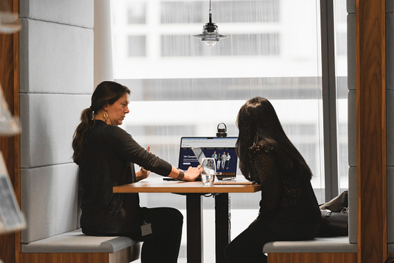 Two colleagues sat in a meeting booth, having a discussion in front of a laptop