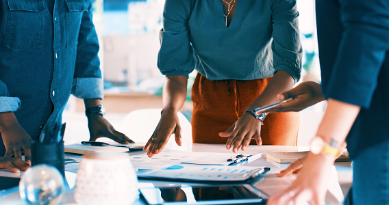 people standing around desk full of papers discussing them