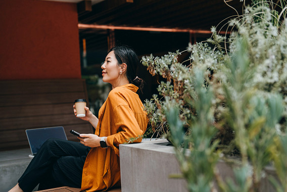 Stylish young woman with smartphone, working on laptop in outdoor co-working space