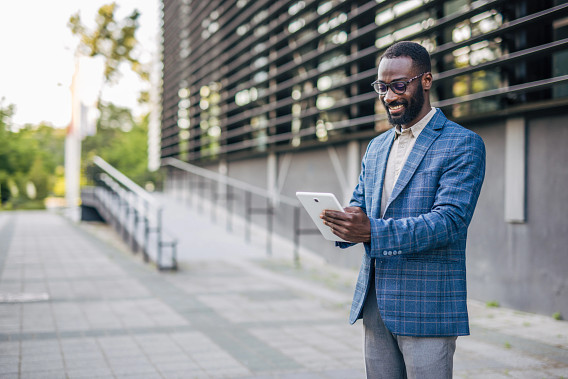 businessperson standing outside a building reading from a tablet device