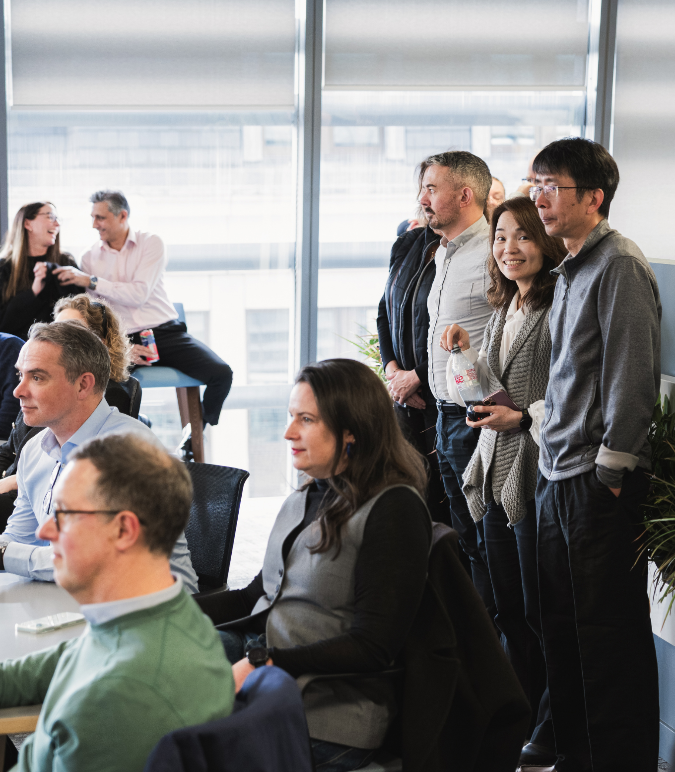 A group of colleagues standing during a team meeting, with a woman smiling at the camera